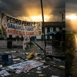Fotografía realista que contrasta una plaza lúgubre llena de basura de vallas electorales en Colombia con un amanecer dorado al fondo que ilumina a Iván Cepeda y Aida Quilqué.