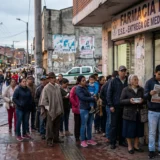 Personas haciendo fila en la calle frente a una farmacia con letrero de 'Entrega de medicamentos' en Colombia.