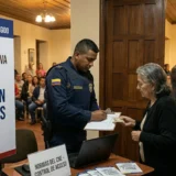 Fotografía documental de un candidato colombiano en un recinto cerrado, hablando apasionadamente desde un podio etiquetado 'COLOMBIA VOTA 2026', durante un encuentro privado antes de las elecciones legislativas. Un banner detrás de él dice 'ENCUENTRO PRIVADO CON CANDIDATOS PARA EL CONGRESO (SENADO Y CÁMARA)'. SEO optimizado para Proclama del Pacífico y elecciones en Colombia. Realistic imagery.