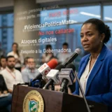 Una líder política en un atril de la Gobernación del Valle del Cauca, Colombia, hablando ante micrófonos mientras se superponen textos flotantes que dicen "FAKE NEWS", "#ViolenciaPolíticaMata", "Ataques digitales" y "Respeto a la Gobernadora".
