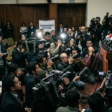 Fotografía de una caótica rueda de prensa en Colombia sobre transparencia electoral, con un político gritando en el podio y periodistas enfocados en él.