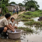 Escena de convivencia en Colombia: un hipopótamo invasor en el río Magdalena cerca de una mujer y un niño lavando ropa en la orilla en el Pacífico colombiano.