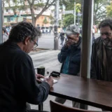 Periodista escribe en cafetería mientras habitantes de calle observan desde la calle