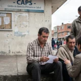 Fotografía documental de un grupo de personas en la entrada de un centro de atención primaria en salud (CAPS) en Colombia.