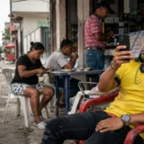 Hombre con camiseta amarilla revisa su celular en una tienda de barrio colombiana