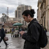 Joven consulta su celular frente a edificio vigilado en una ciudad colombiana