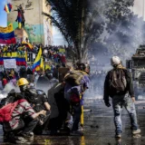 Manifestantes con banderas de Colombia durante protestas y enfrentamientos con un vehículo antimotines en una vía urbana.
