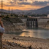 Embalse afectado por sequía con infraestructura energética y campesino observando el paisaje