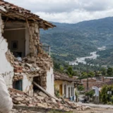 Mujer contempla una vivienda deteriorada frente a un paisaje montañoso